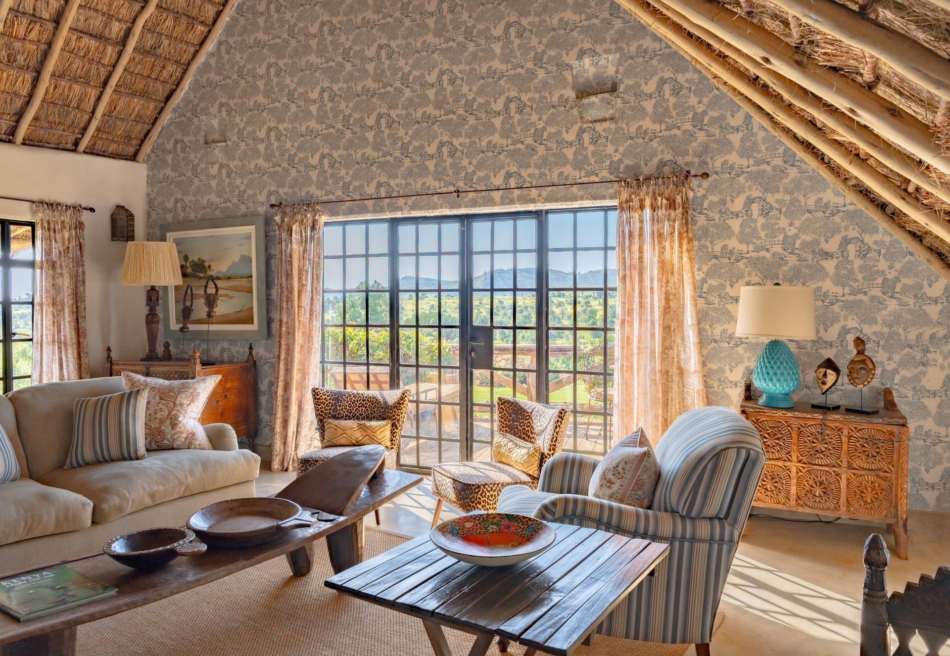 Cozy rustic living room with thatched ceiling, sofa, coffee table, and large window overlooking greenery