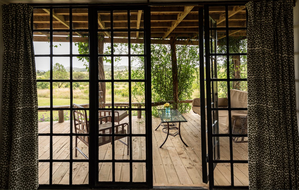 Open patio doors framing a wooden deck with chair and lush greenery outside