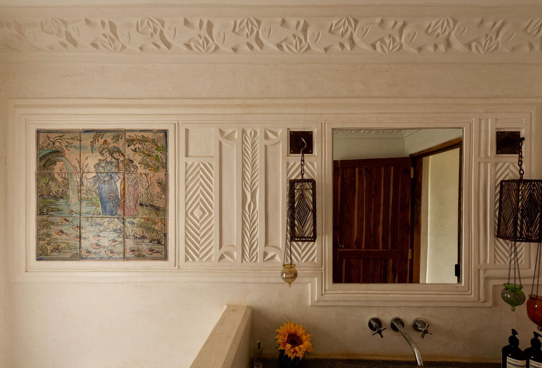 Cream bathroom wall with framed map, mirror, tiled décor, and a sink with a sunflower.