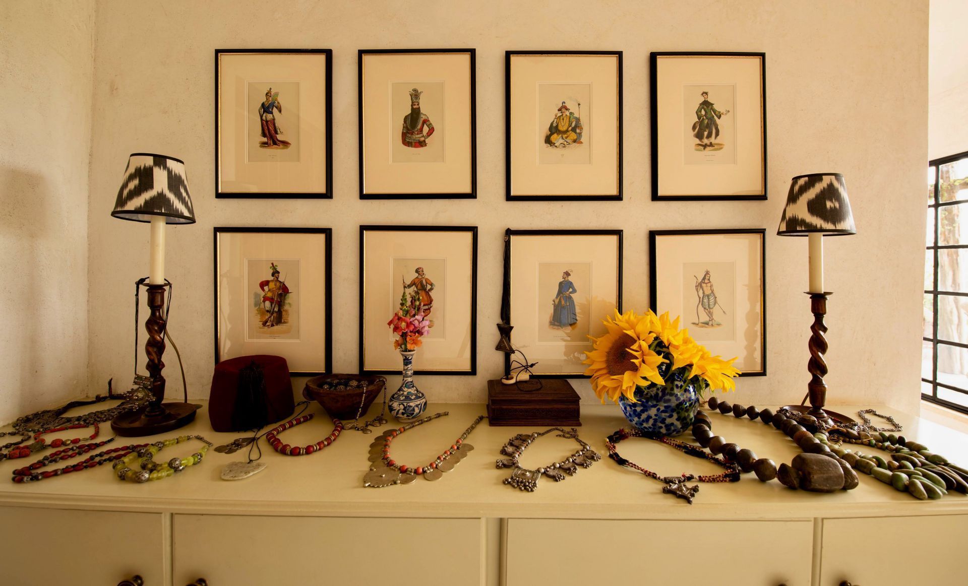 Decorative mantel with framed art, vintage hats, flowers, and braided cords in a warm, beige room