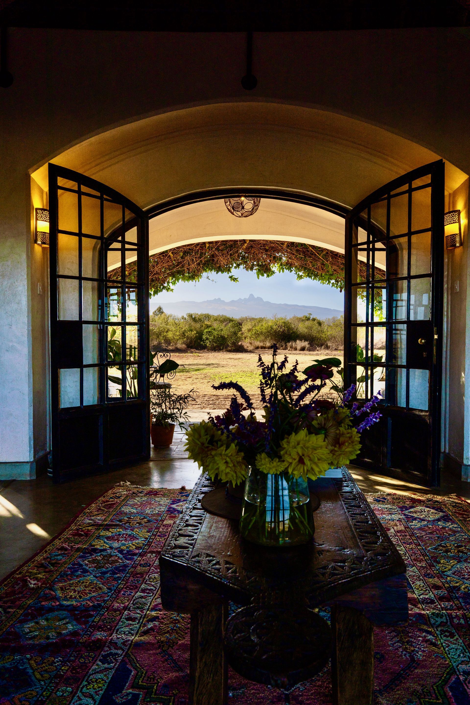 Open doors frame a bright desert view, with a table and flowers in the dim interior.