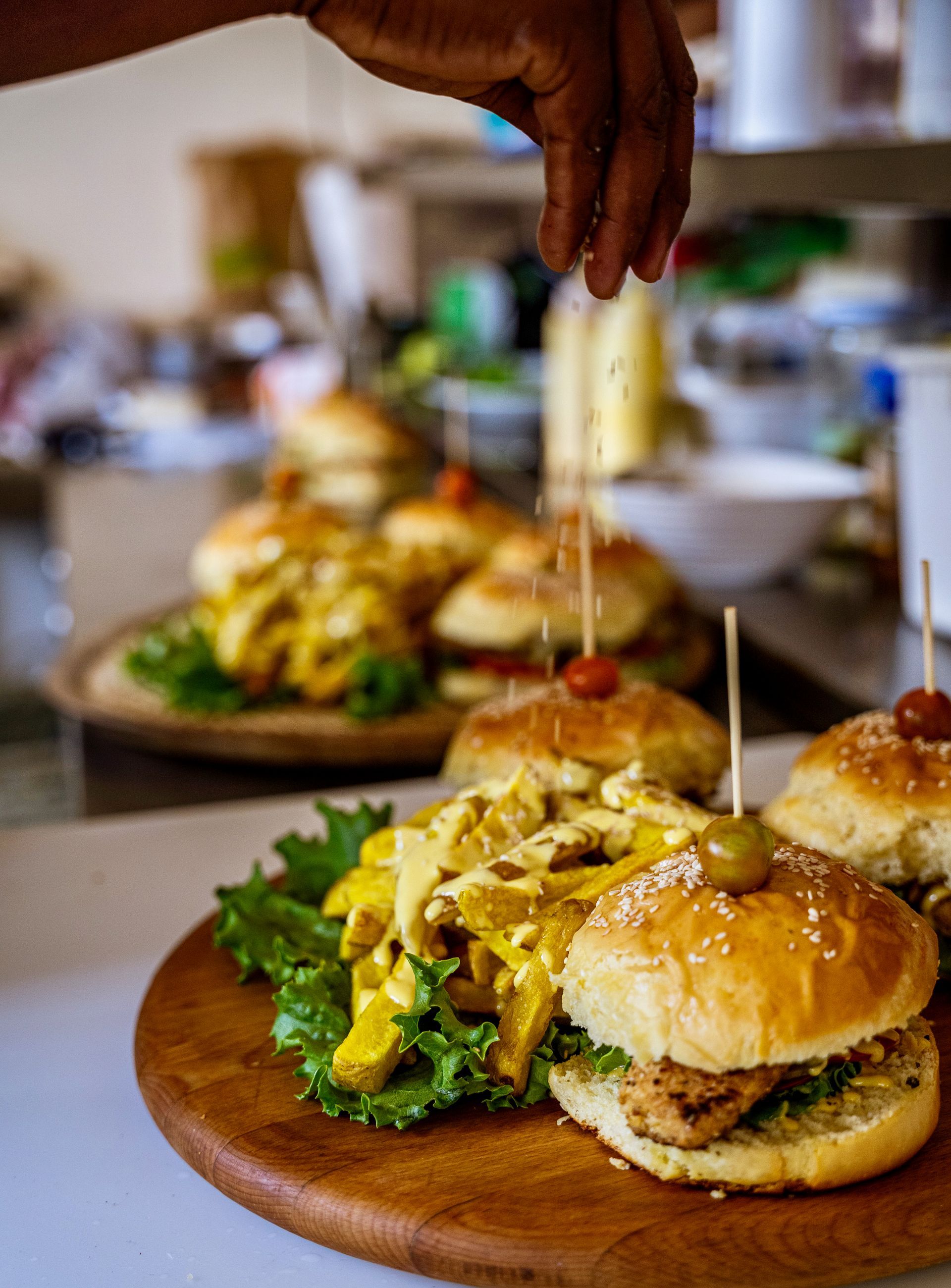 Hand placing a garnish on a plate of gourmet sliders and fries on a restaurant table