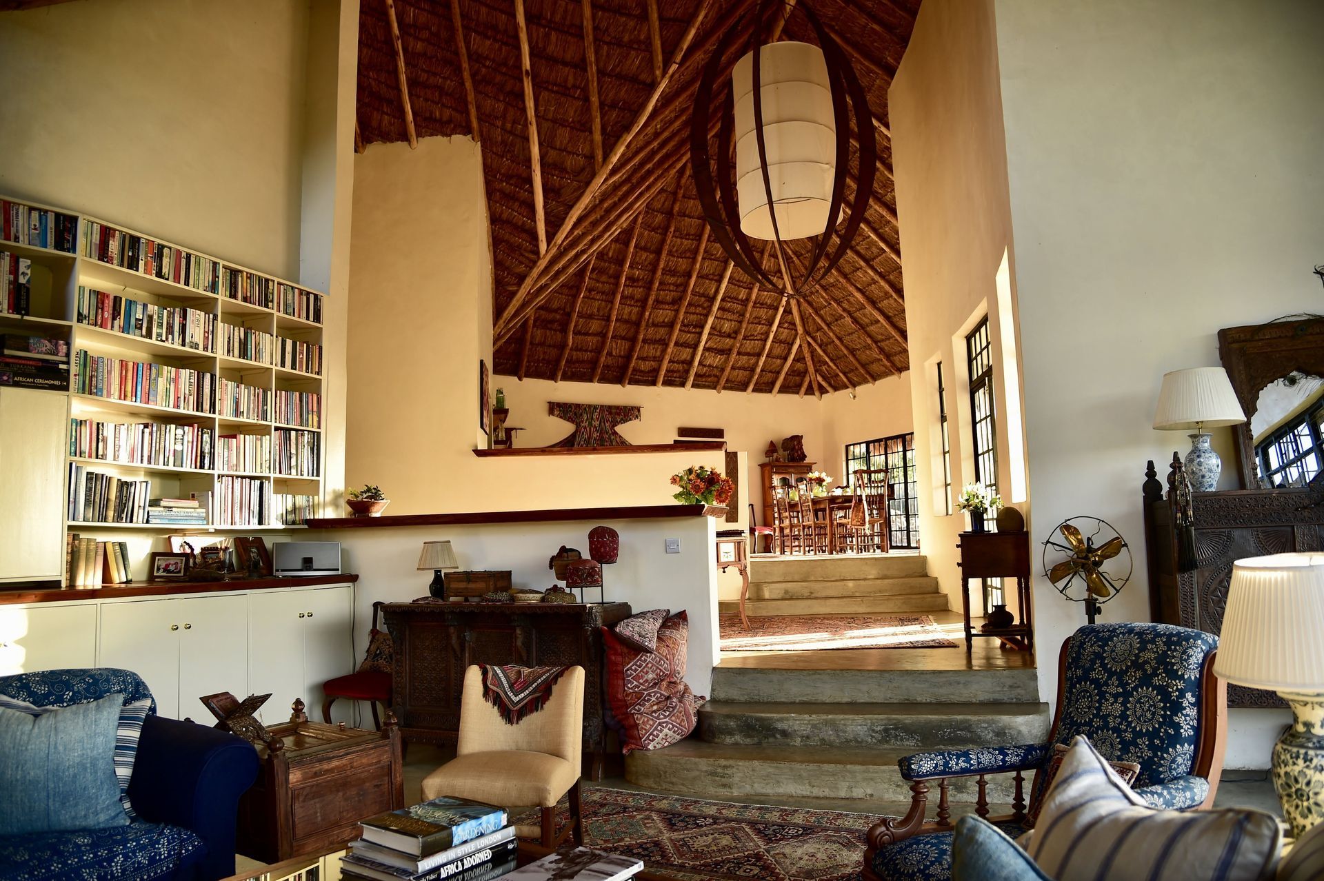 Cozy living room with woven ceiling, patterned rugs, bookshelves, and eclectic chairs around a central seating area
