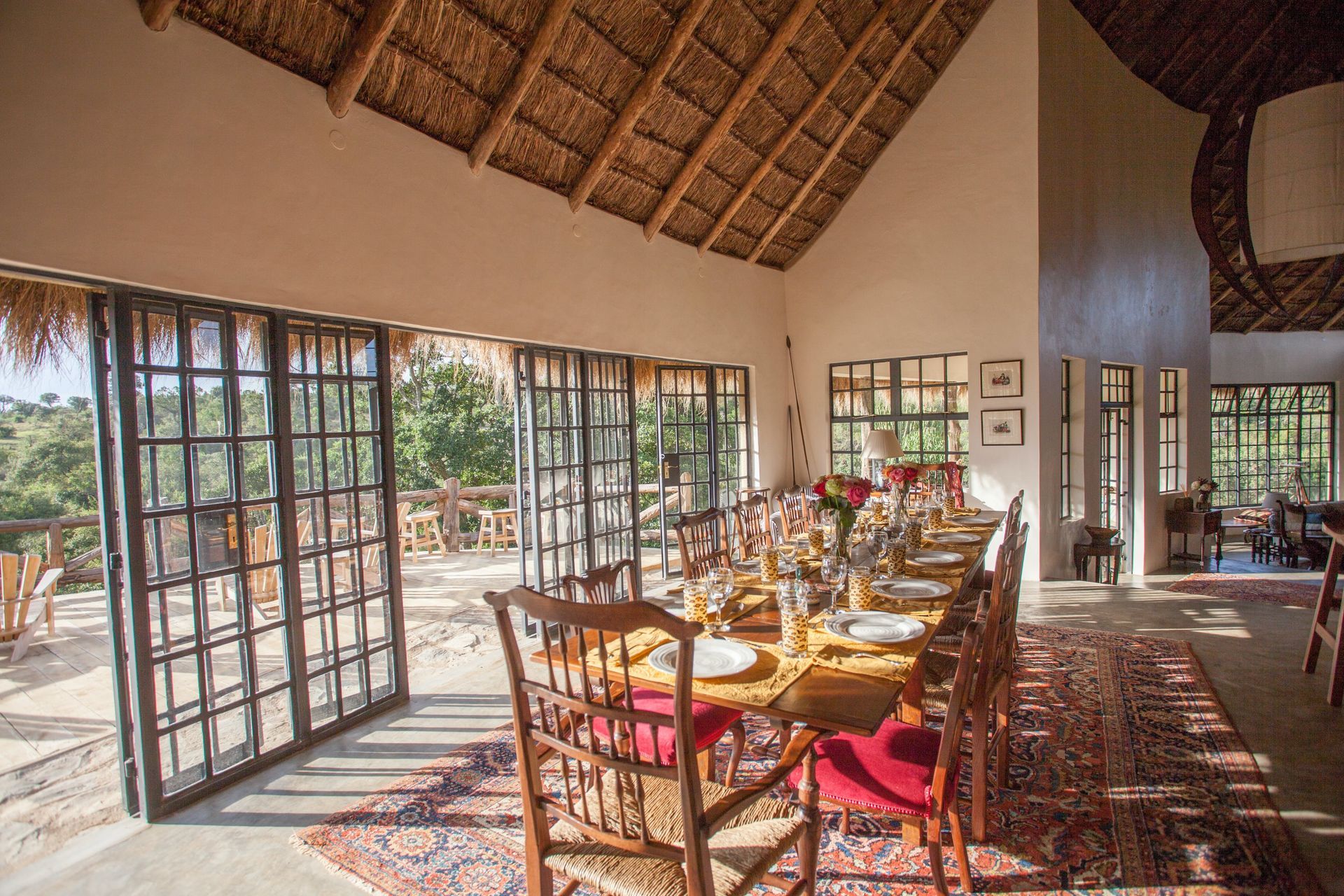 Open-air restaurant with wooden tables, woven chairs, and thatched roof, overlooking greenery through wide windows