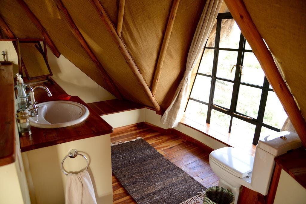 Small attic bathroom with sink, toilet, rug, and slanted wood-paneled ceiling beside a window.