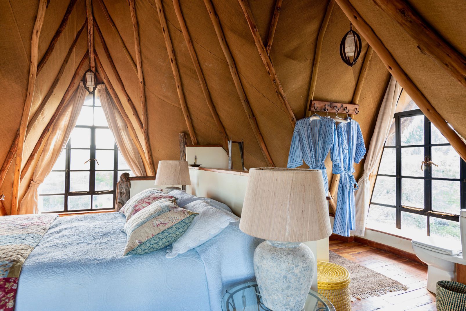 Cozy tent bedroom with a bed, lamps, plaid robe, and windows on both sides