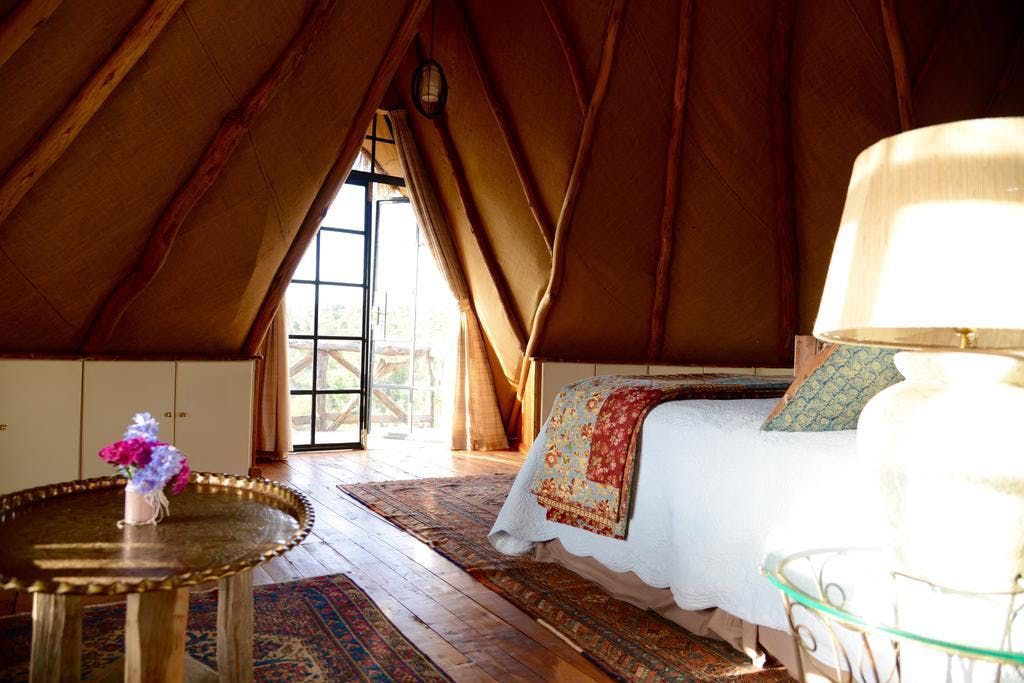 Cozy tented bedroom with a bed, lamp, patterned rug, and wooden table by a window.