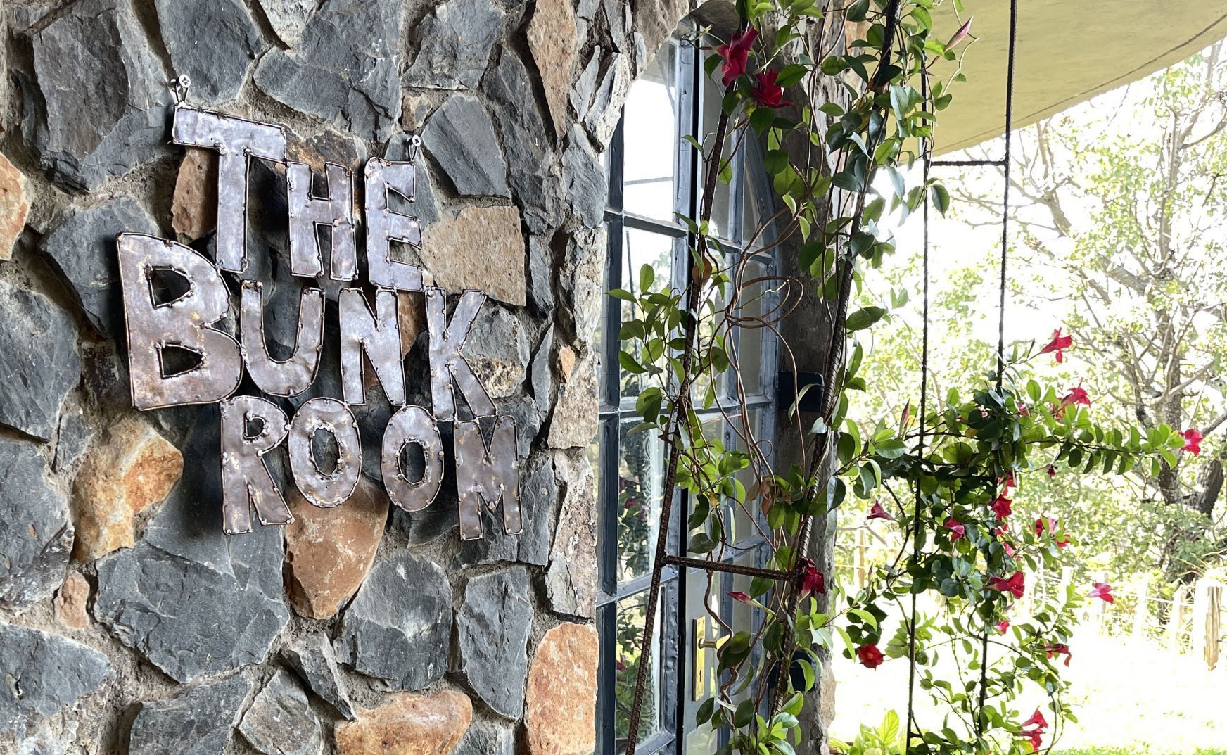 Stone wall sign reading “The Bunk Room” beside an arched gate with hanging flowers.