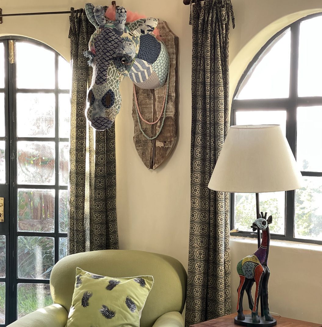 Cozy corner with arched windows, green chair, patterned curtains, table lamp, and decorative wall art
