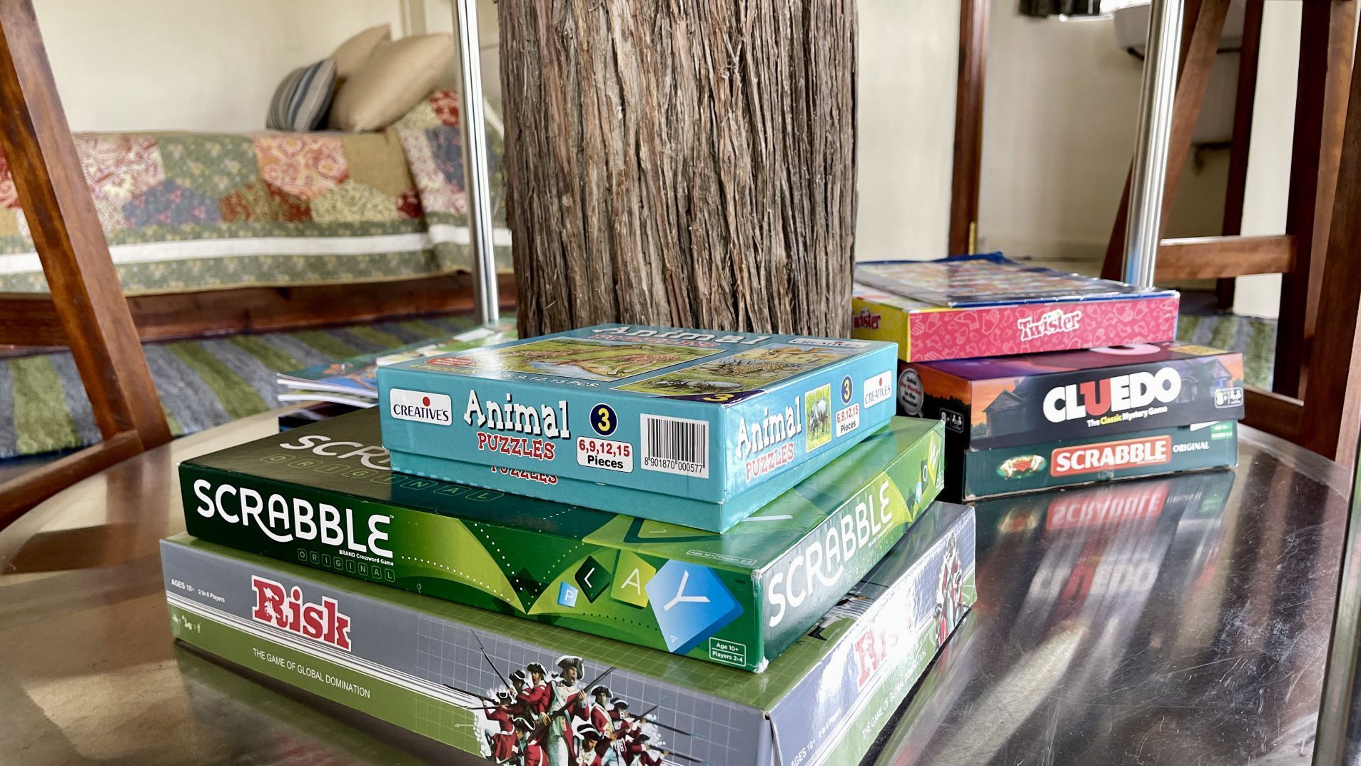 Stack of colorful board games on a glass table in a living room with a tree trunk centerpiece