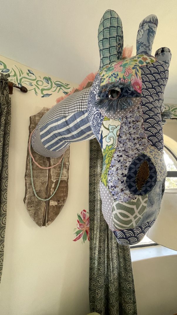 Colorful mosaic giraffe sculpture indoors against a cream wall