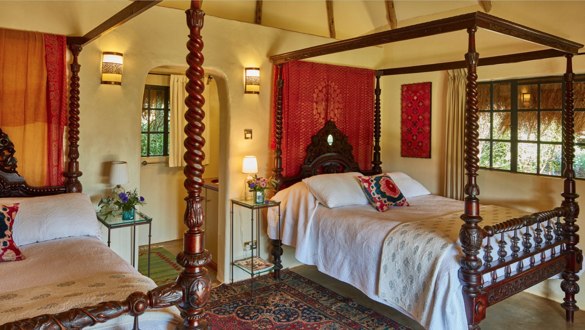 Cozy bedroom with two canopy beds, red accents, warm lighting, and patterned rugs