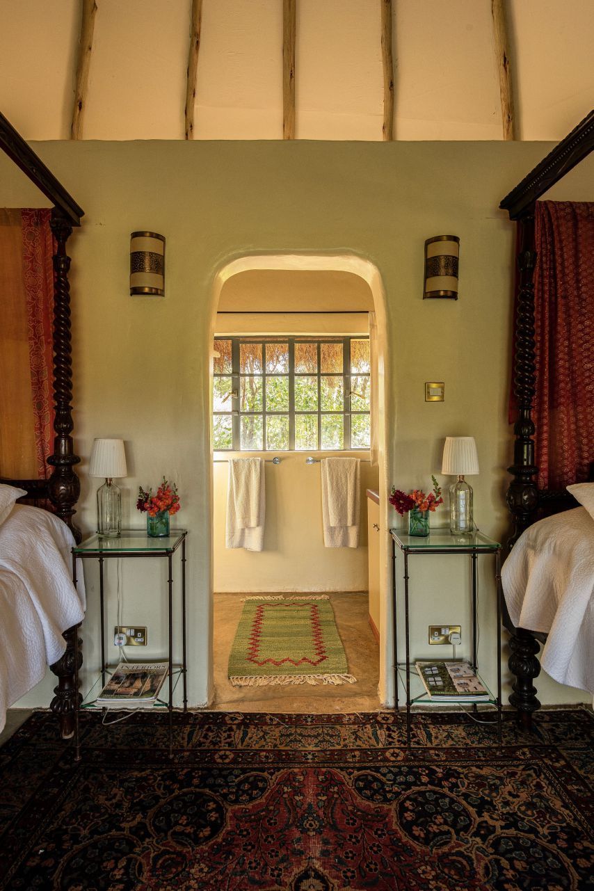 Cozy bedroom with twin beds, patterned rug, and arched doorway to a bright bathroom or sitting area.