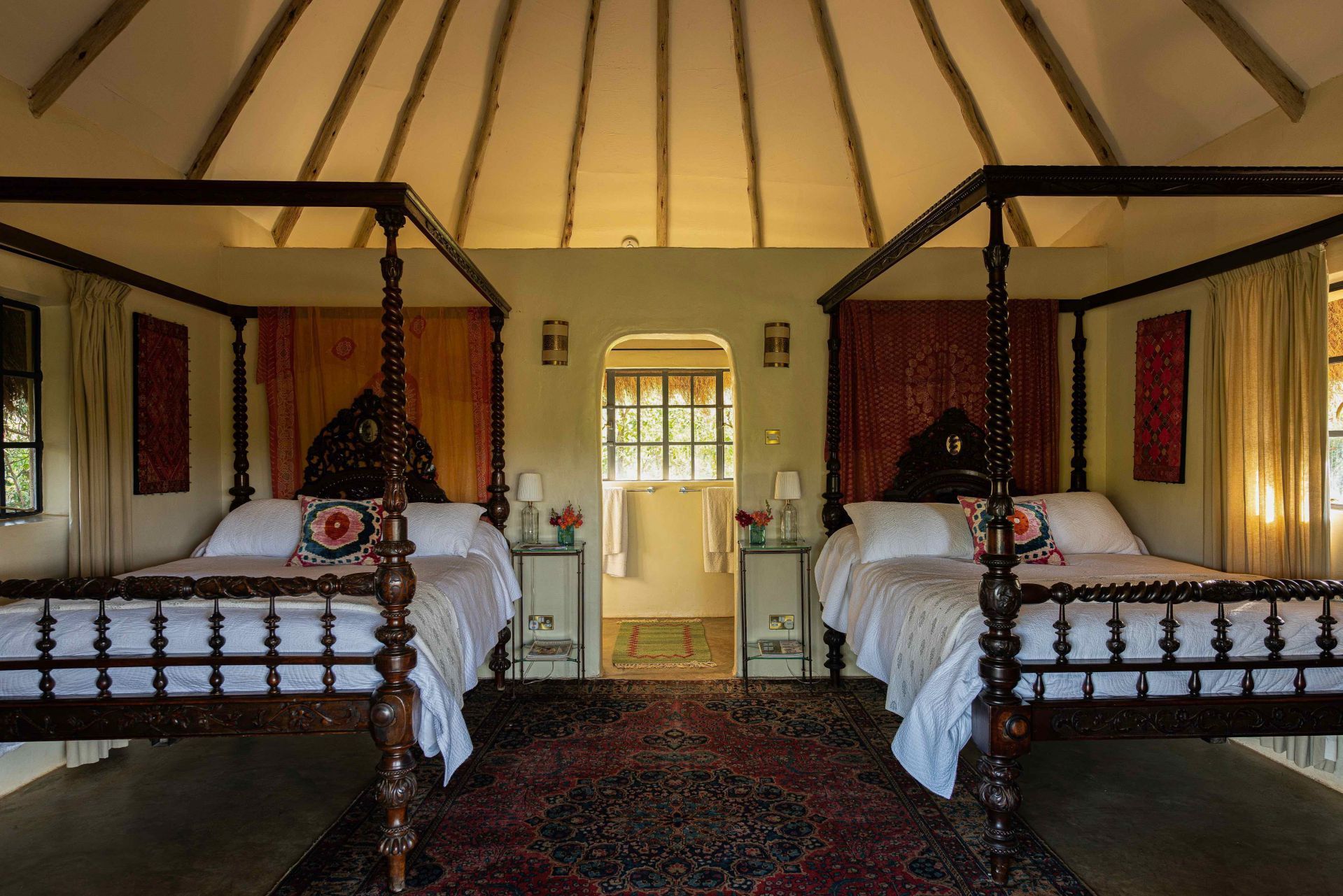 Twin beds in a rustic tent-style room with patterned rugs and a central doorway