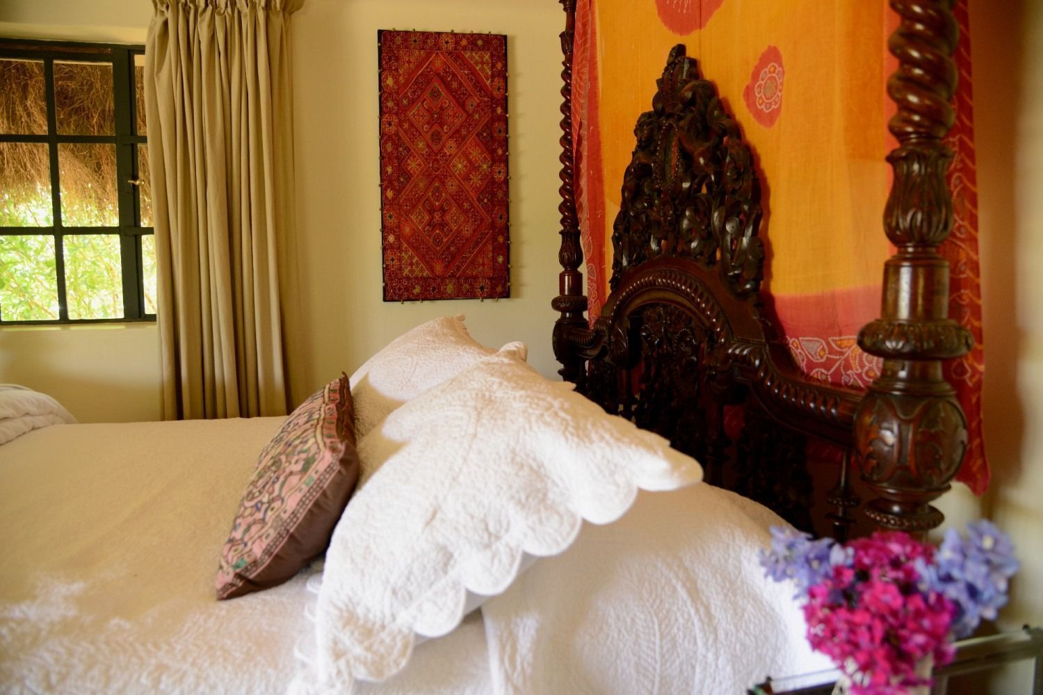 Cozy bedroom with a carved dark wood bed, white bedding, floral accents, and warm orange walls