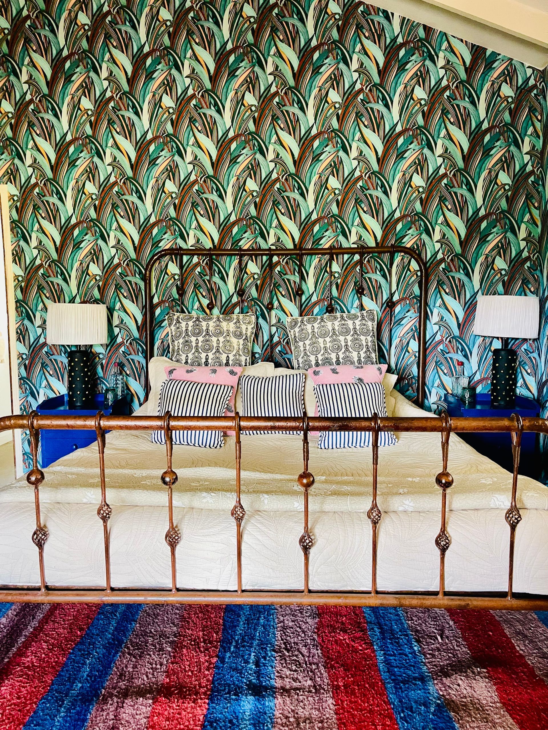 Bedroom with patterned wallpaper, brass bed, matching lamps, and striped rug