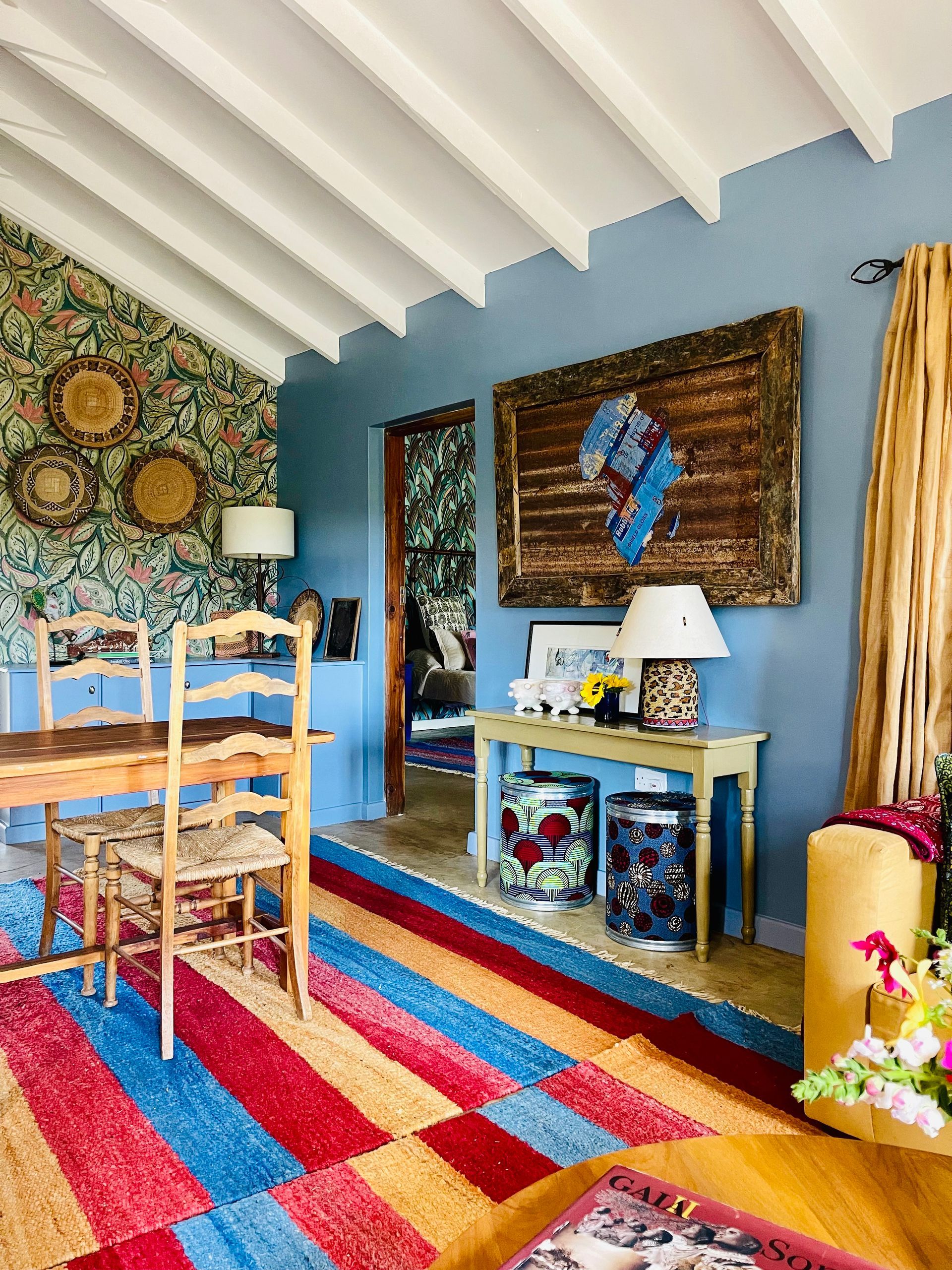 Colorful dining room with striped rug, blue walls, woven wall art, and a white table and chairs.