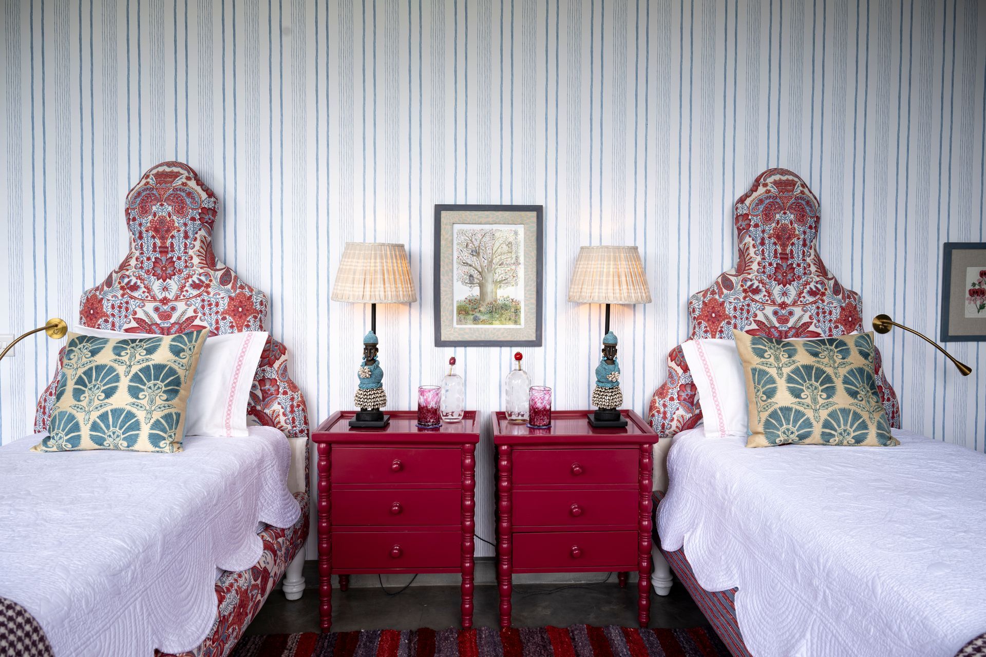 Twin beds with floral headboards, red nightstands, and striped wallpaper in a bright bedroom