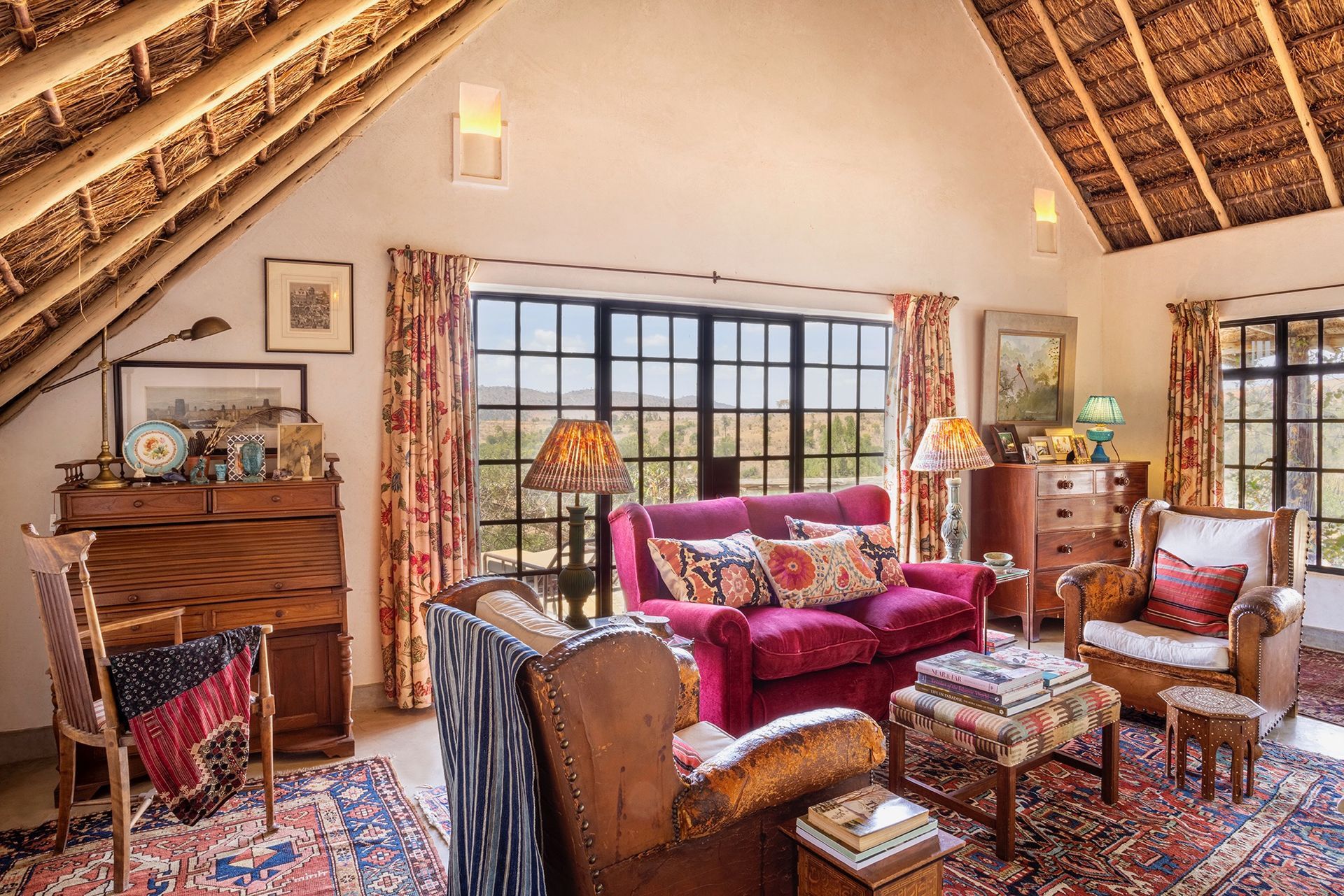 Cozy living room with pink sofa, patterned chairs, rug, and exposed wood-beam ceiling by large windows