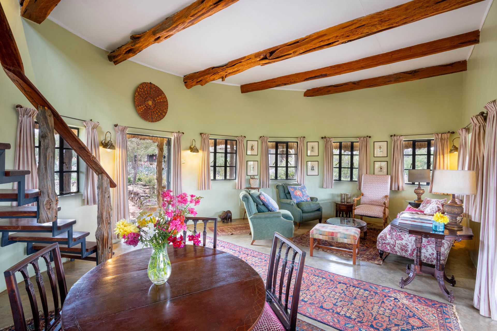 Cozy rustic living room with exposed beams, green walls, floral decor, and wooden furniture