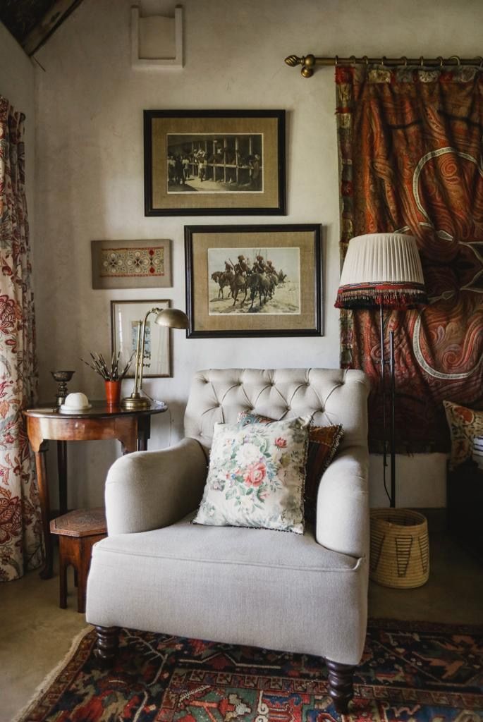 Cozy living room with a tufted armchair, floral pillow, vintage wall art, and patterned curtains