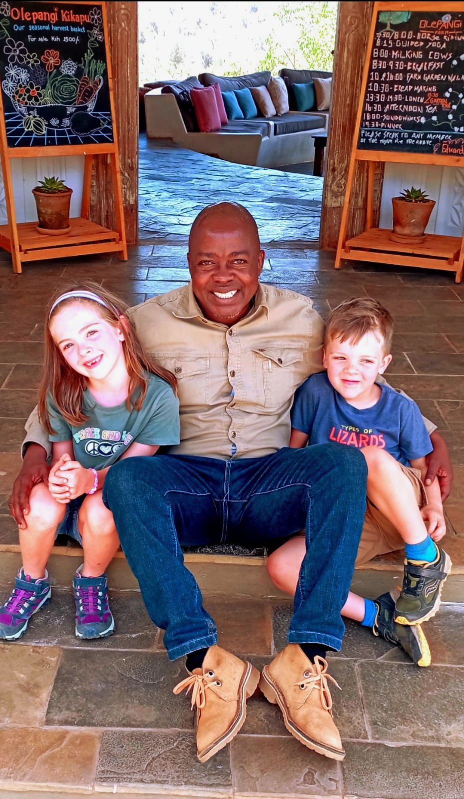 Three people sitting on a bench in a rustic indoor space, smiling with arms around each other.