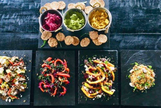 Four colorful vegetable dips with chips on a dark table, arranged on black plates and small bowls.