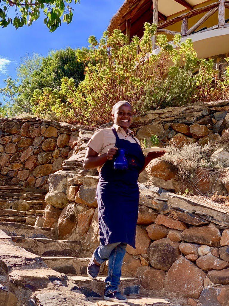 Person in blue overalls walking down stone steps beside a stone wall and garden in bright sunlight