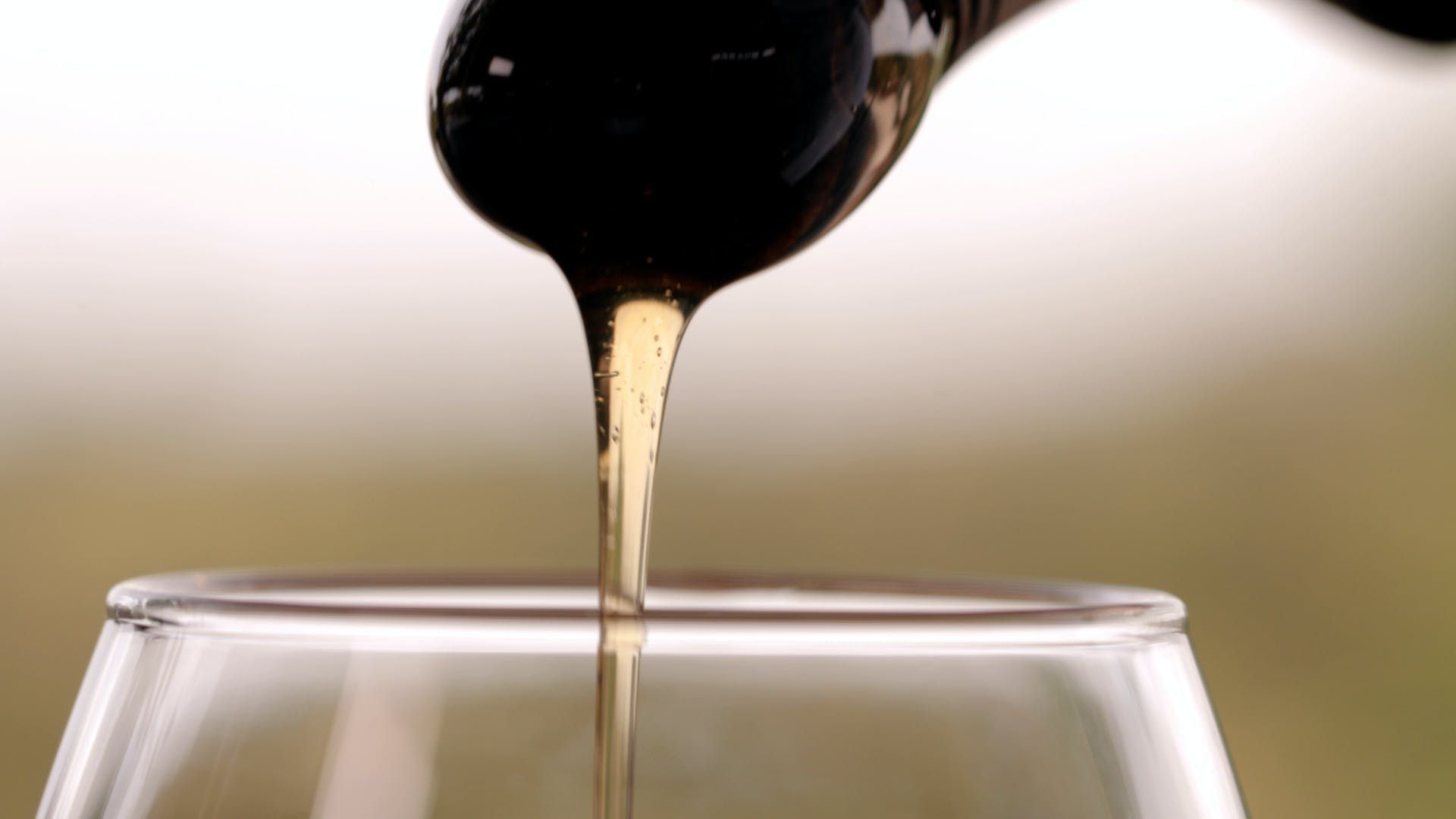 Dark liquid pouring from a spoon into a glass against a blurred background.