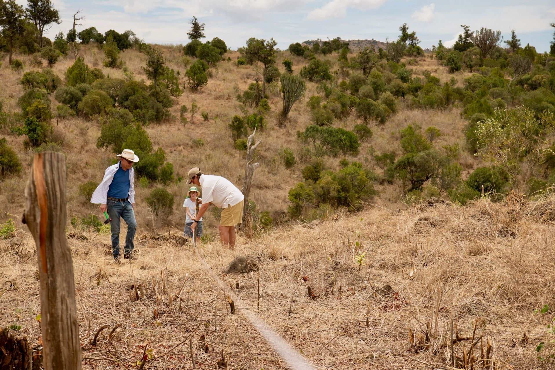 Three people hiking on a dry hillside with scrub and a fence post.
