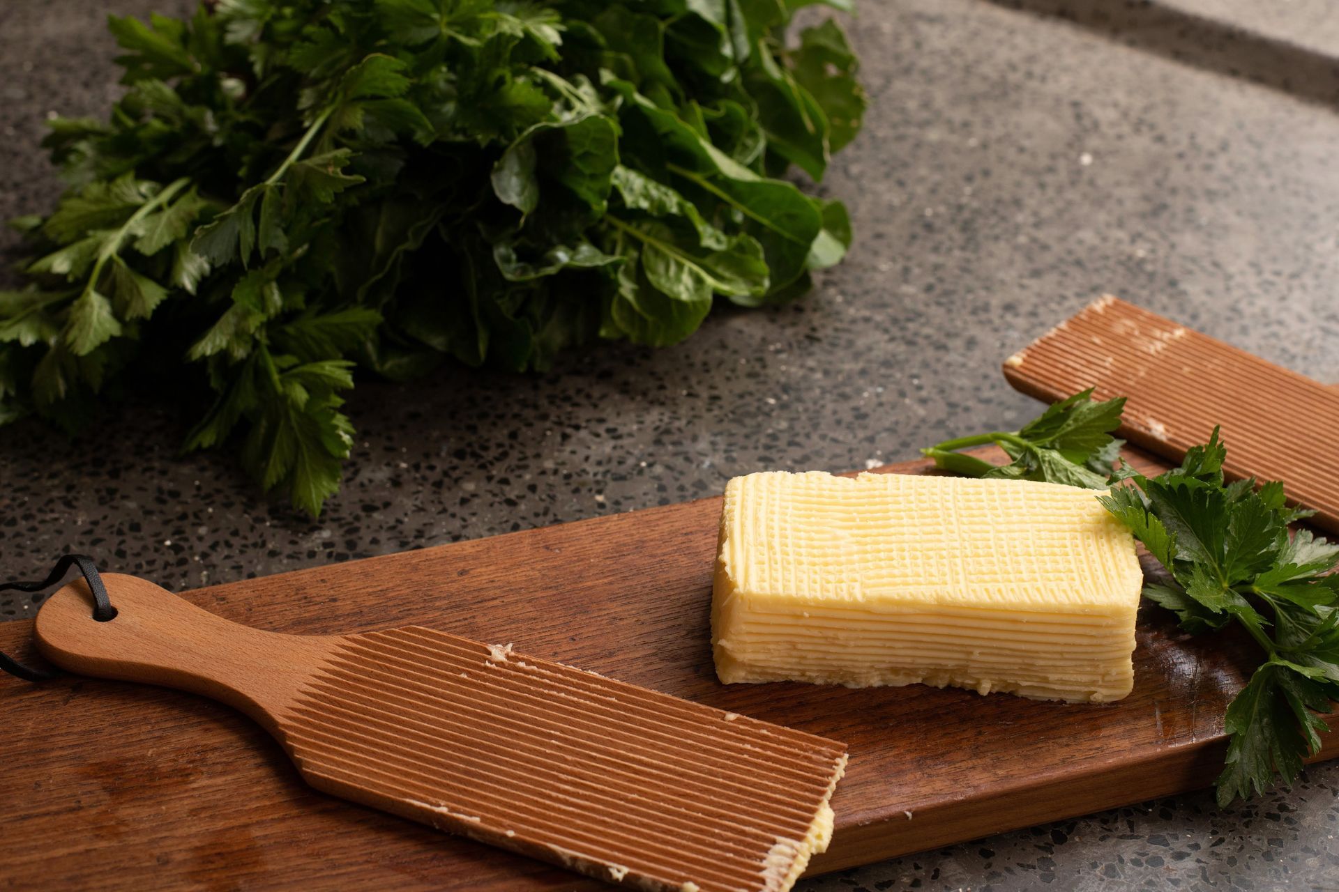 Butter stick on a wooden board with fresh parsley on a gray stone surface