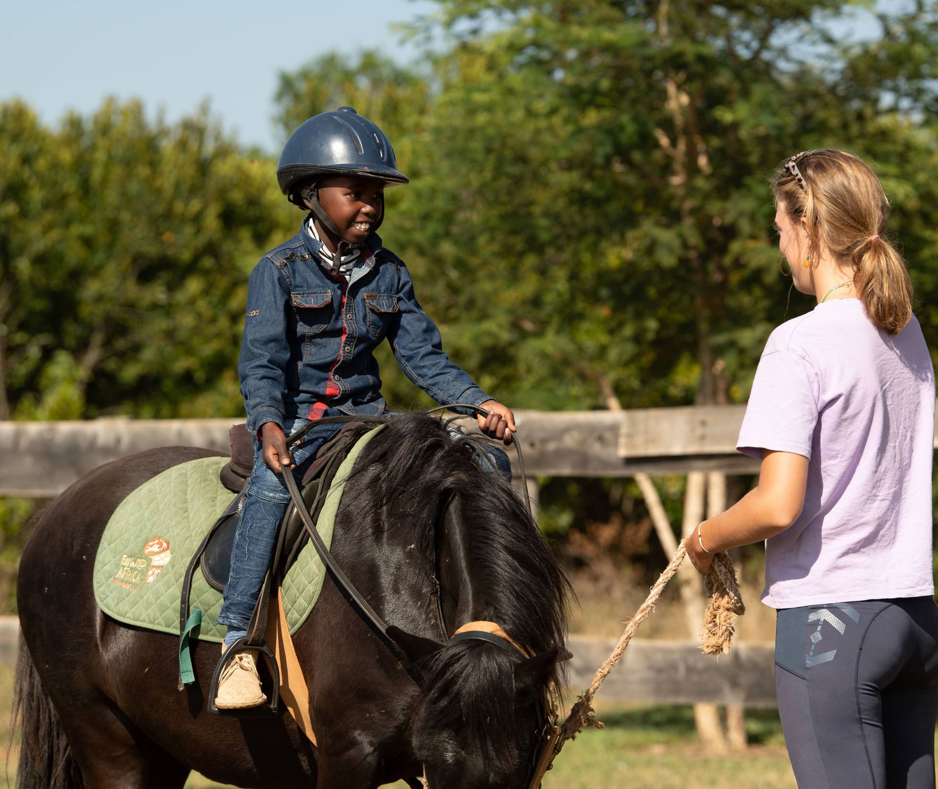 Child riding a black horse while a trainer stands nearby in an outdoor arena