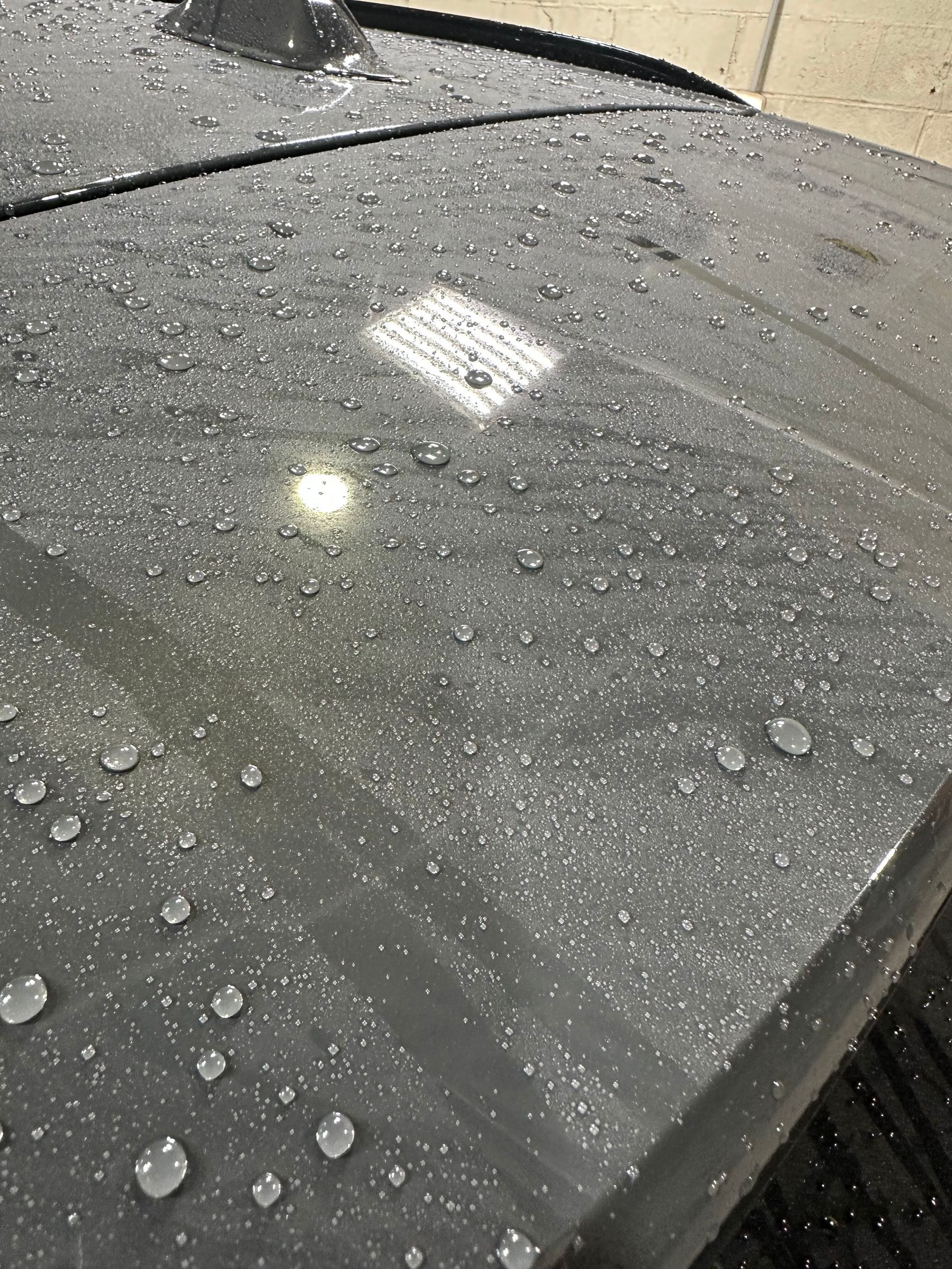 Raindrops beaded on the gray surface of a car roof.
