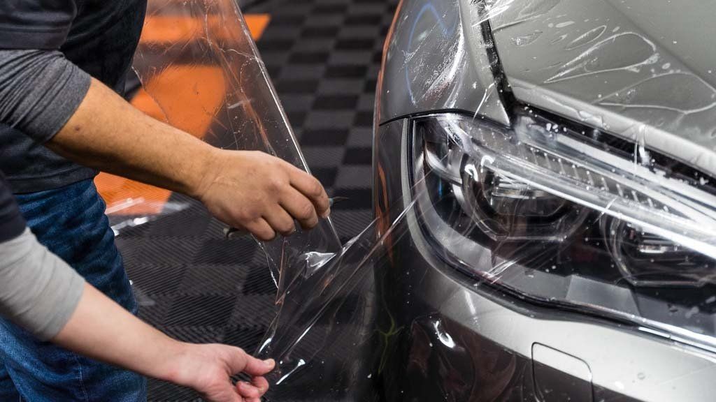 A man is applying a protective film to the front of a car.