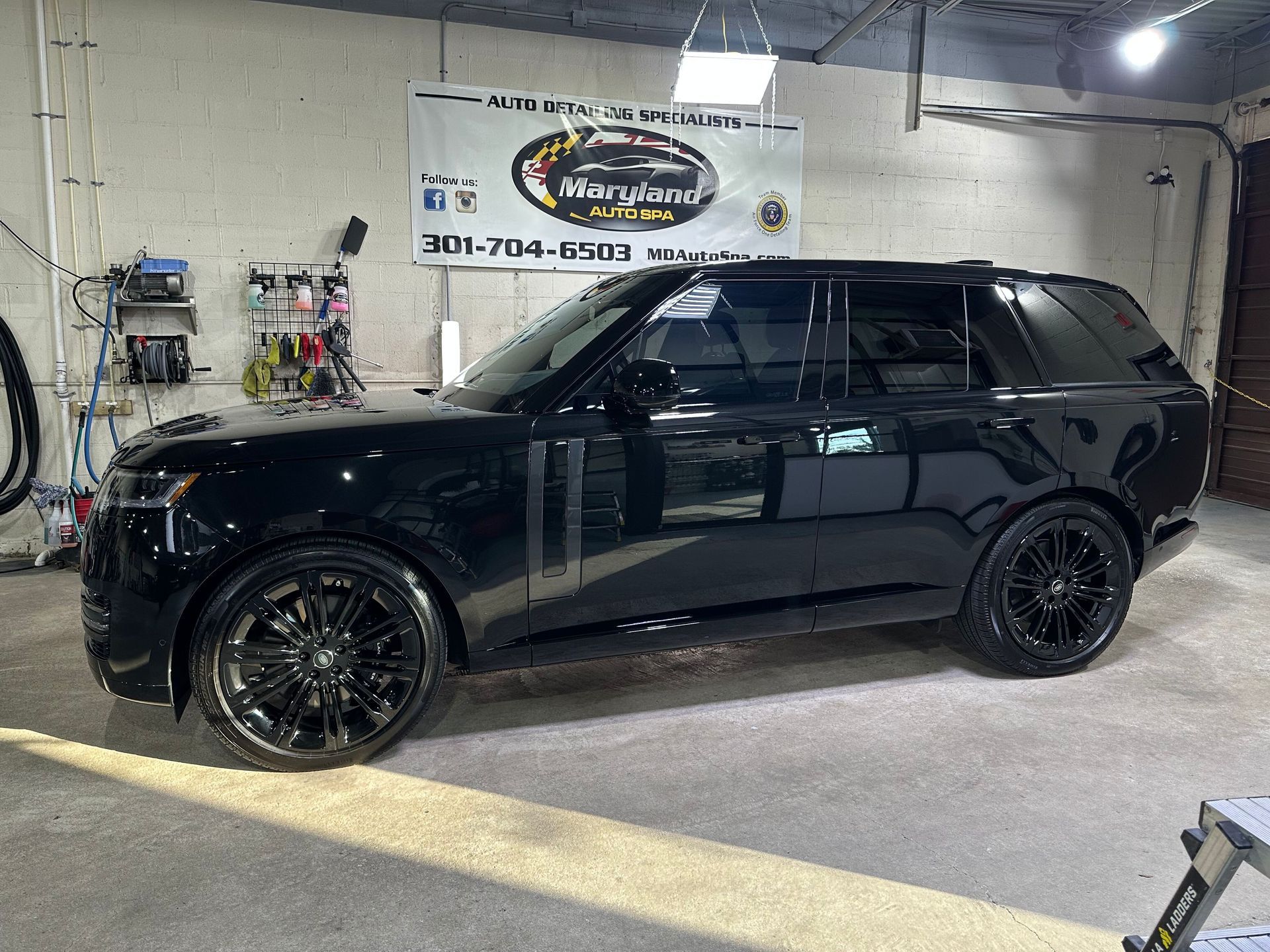 A black Range Rover parked inside a garage with a Maryland Auto Spa banner hanging on the back wall.