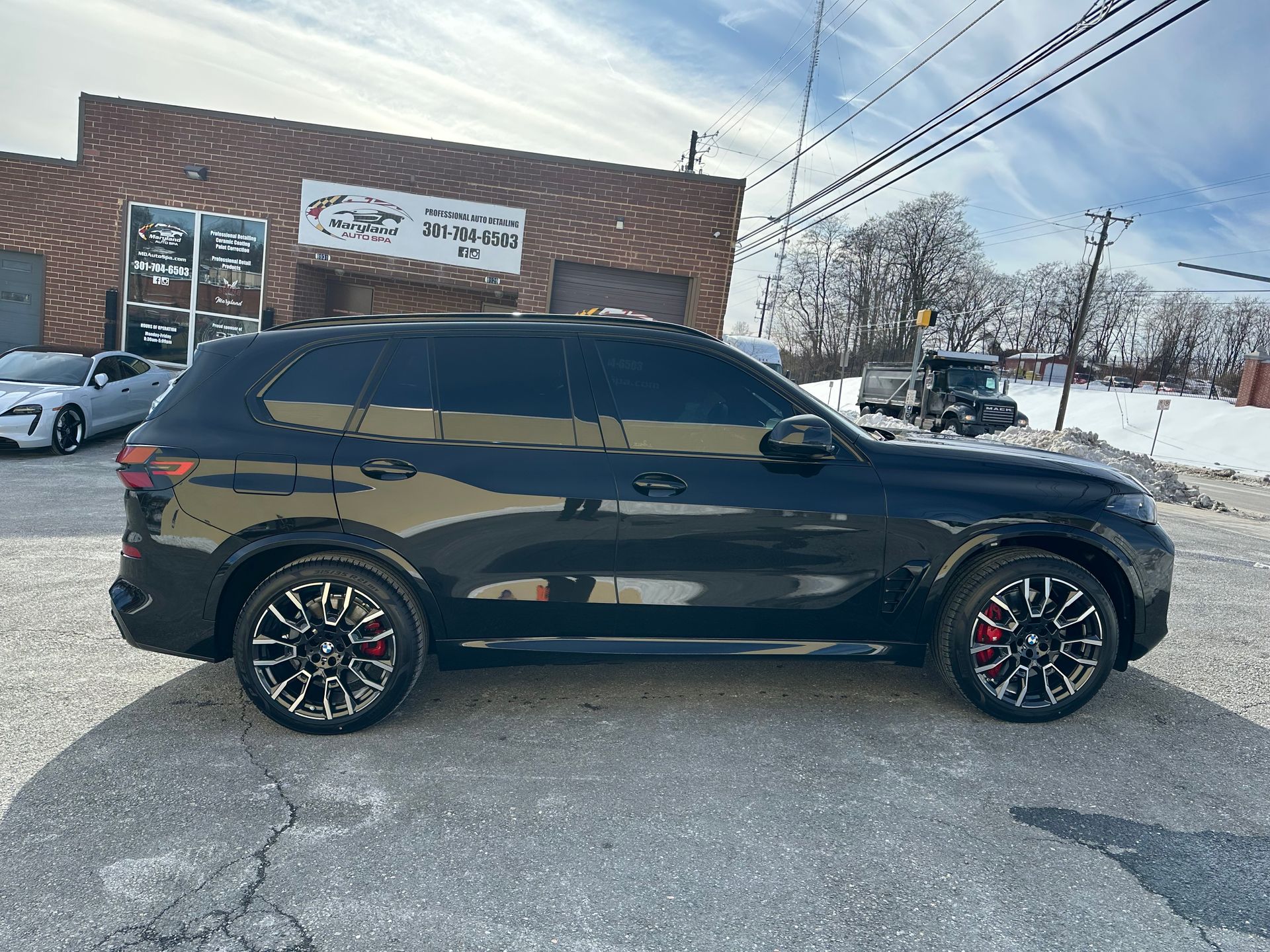 A side profile of a black SUV parked on a snowy gravel lot in front of a brick commercial building.