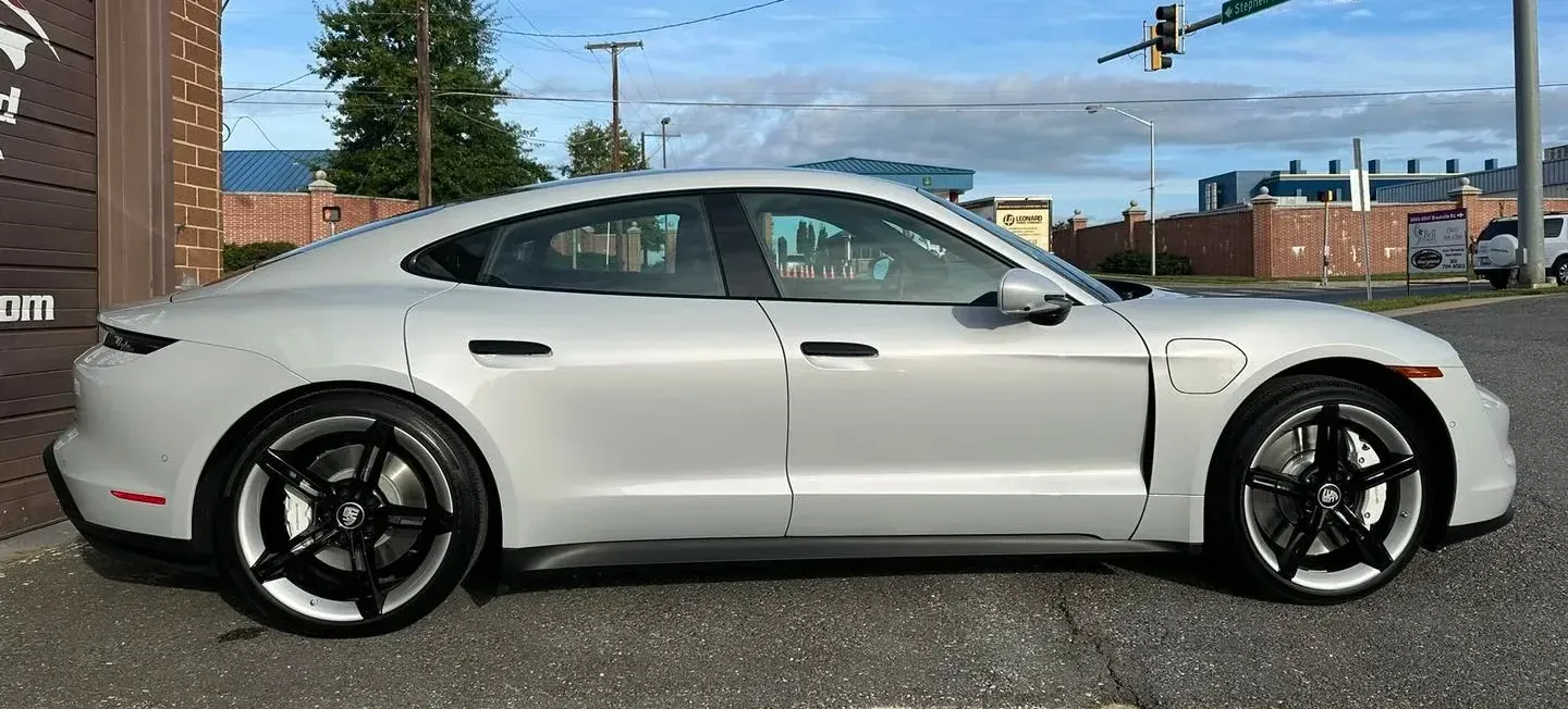 A white porsche taycan is parked in a parking lot in front of a building.