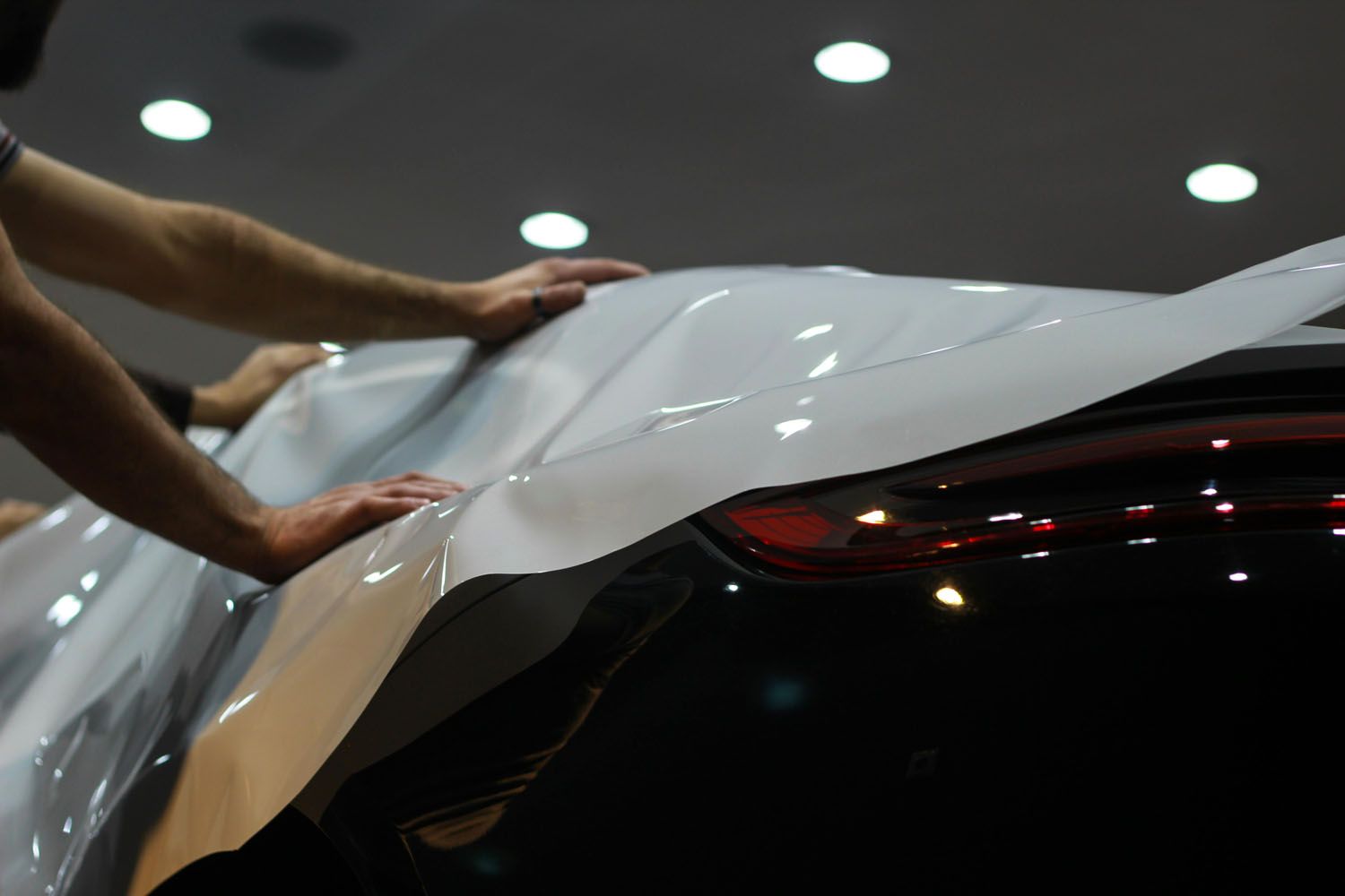Hands peeling white protective film from a black car in a showroom