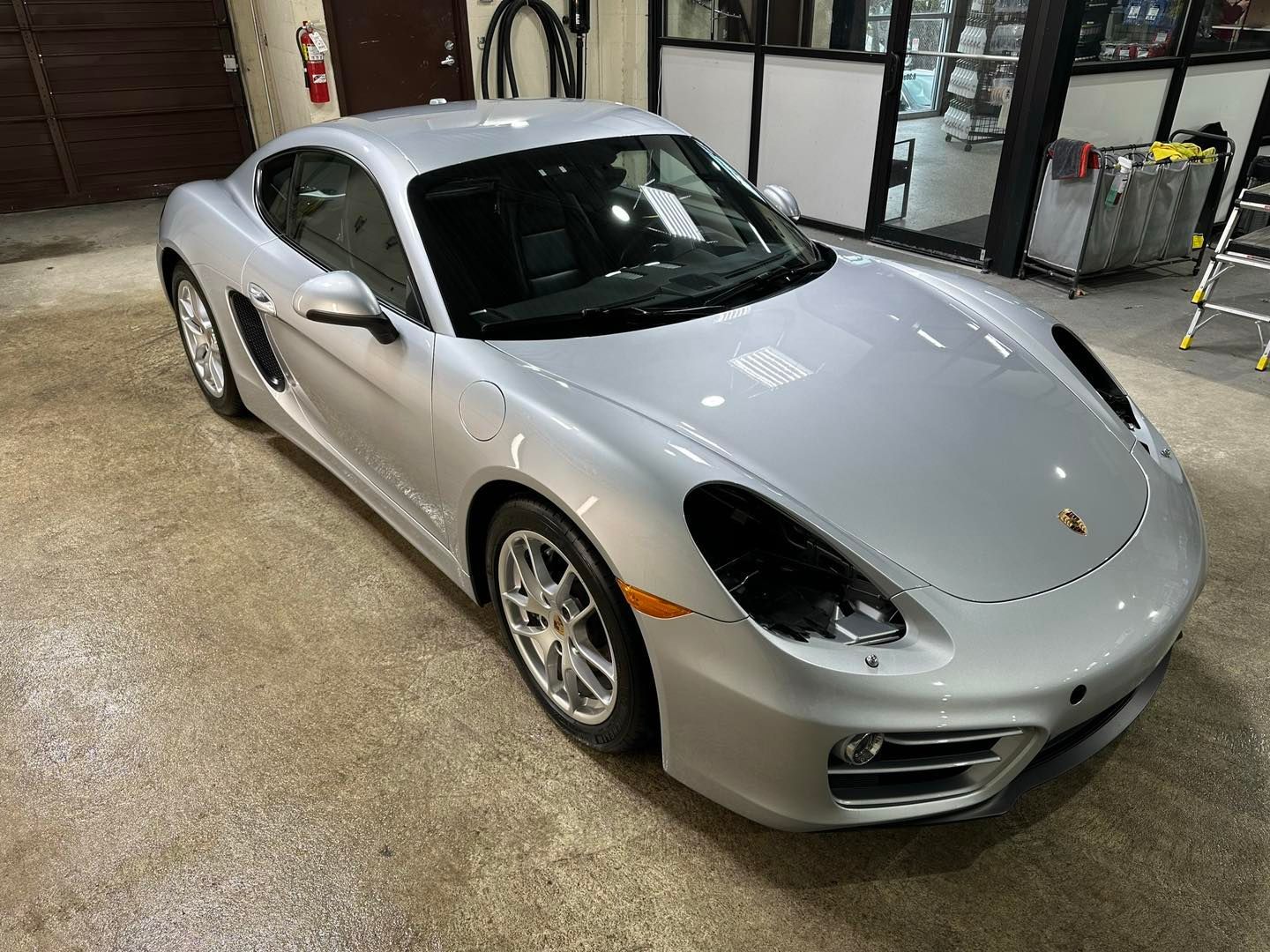 A silver porsche boxster is parked in a garage.