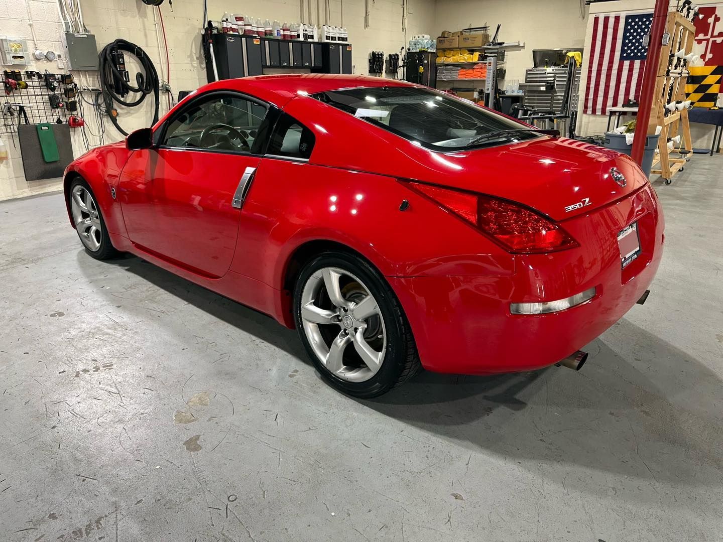 A red sports car is parked in a garage next to an american flag.