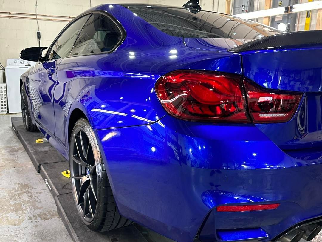 A blue bmw m4 is parked on a ramp in a garage.