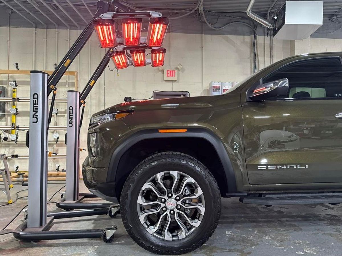 A green truck is parked under a red light in a garage.
