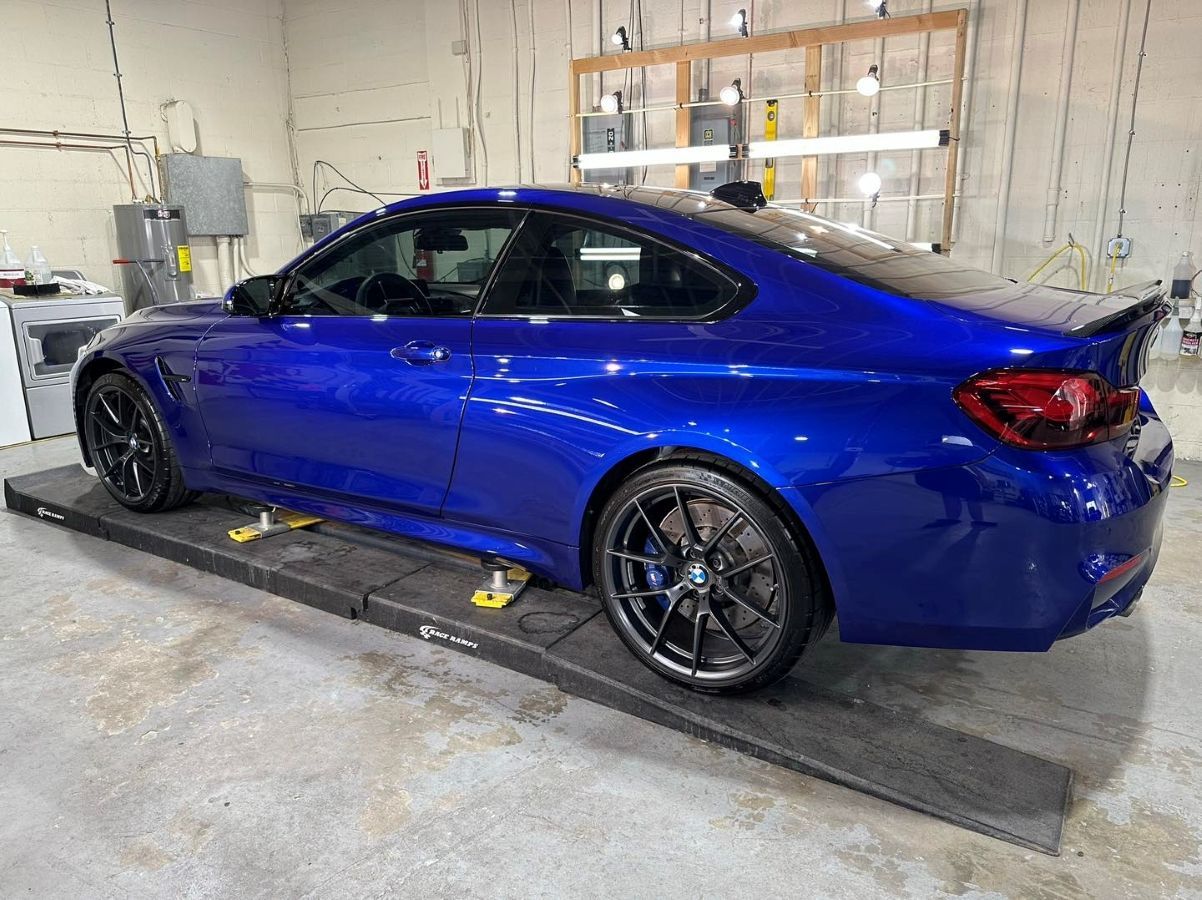 A blue bmw m4 is parked on a ramp in a garage.