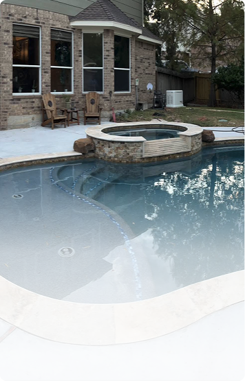 Backyard pool with a circular stone hot tub beside a brick house and patio.