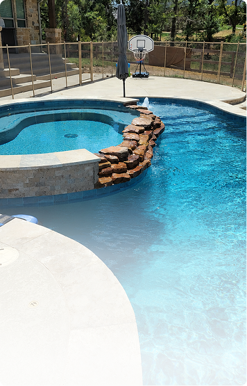 Backyard pool with curved blue water, white deck, and stone waterfall feature