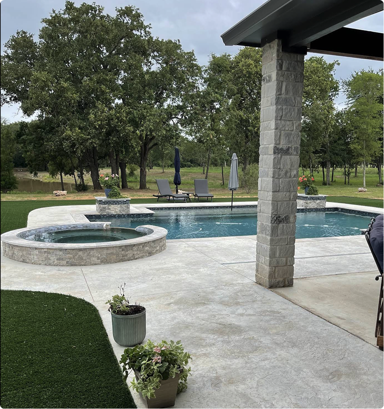 Backyard pool with stone hot tub, patio, trees, and covered porch in the foreground