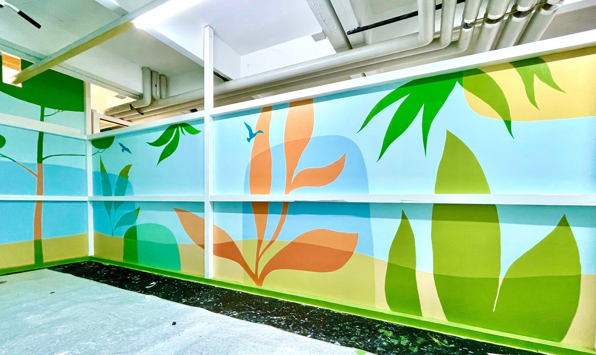 Bright mural of green leaves and orange plants painted on a wall in a covered outdoor walkway