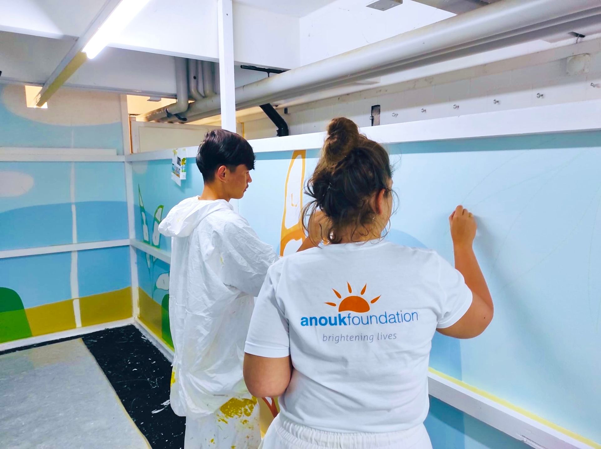 Two people painting a light blue wall in a white room with an orange-capped ladder