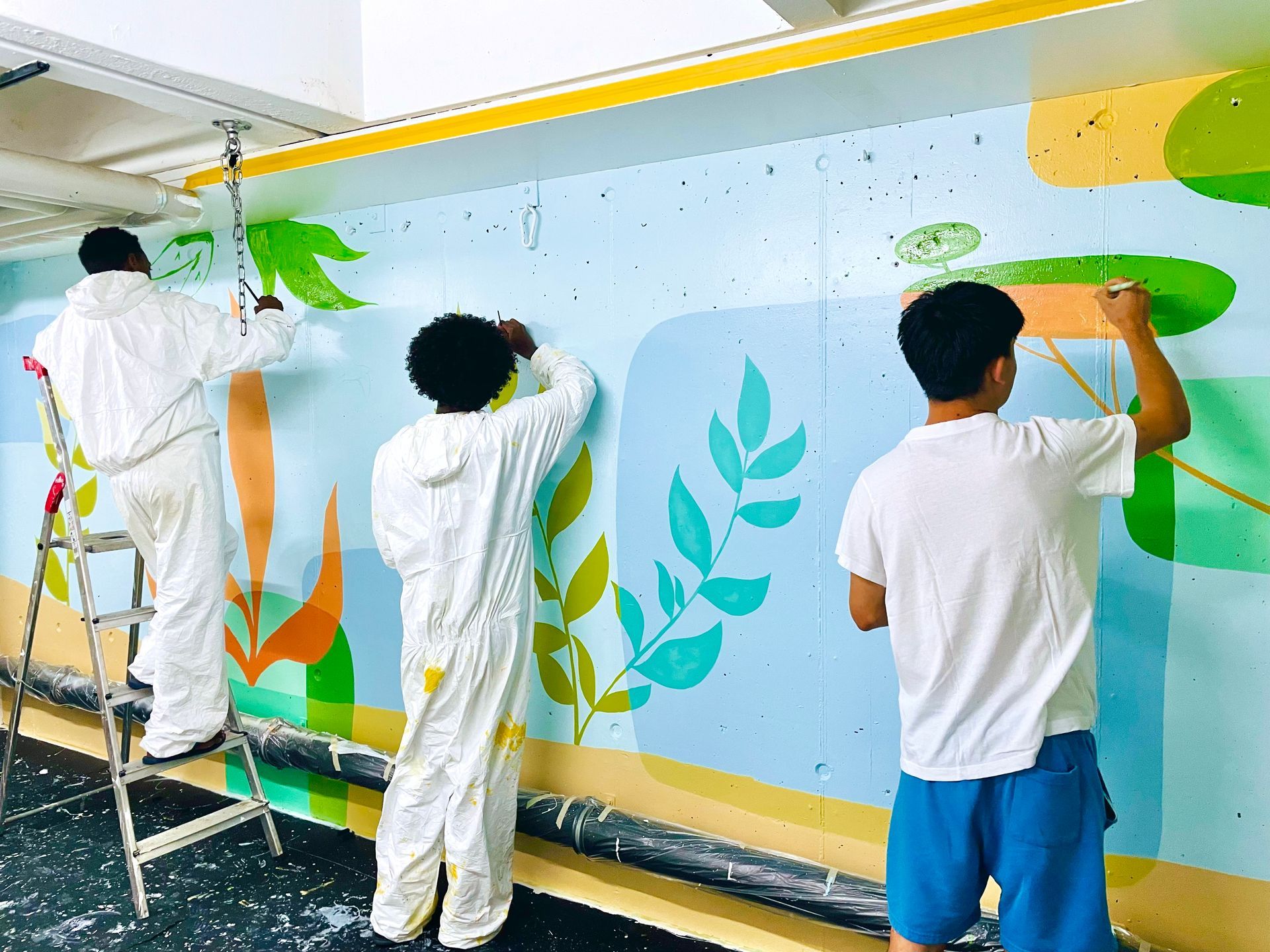 Three people painting a colorful mural on a long wall indoors