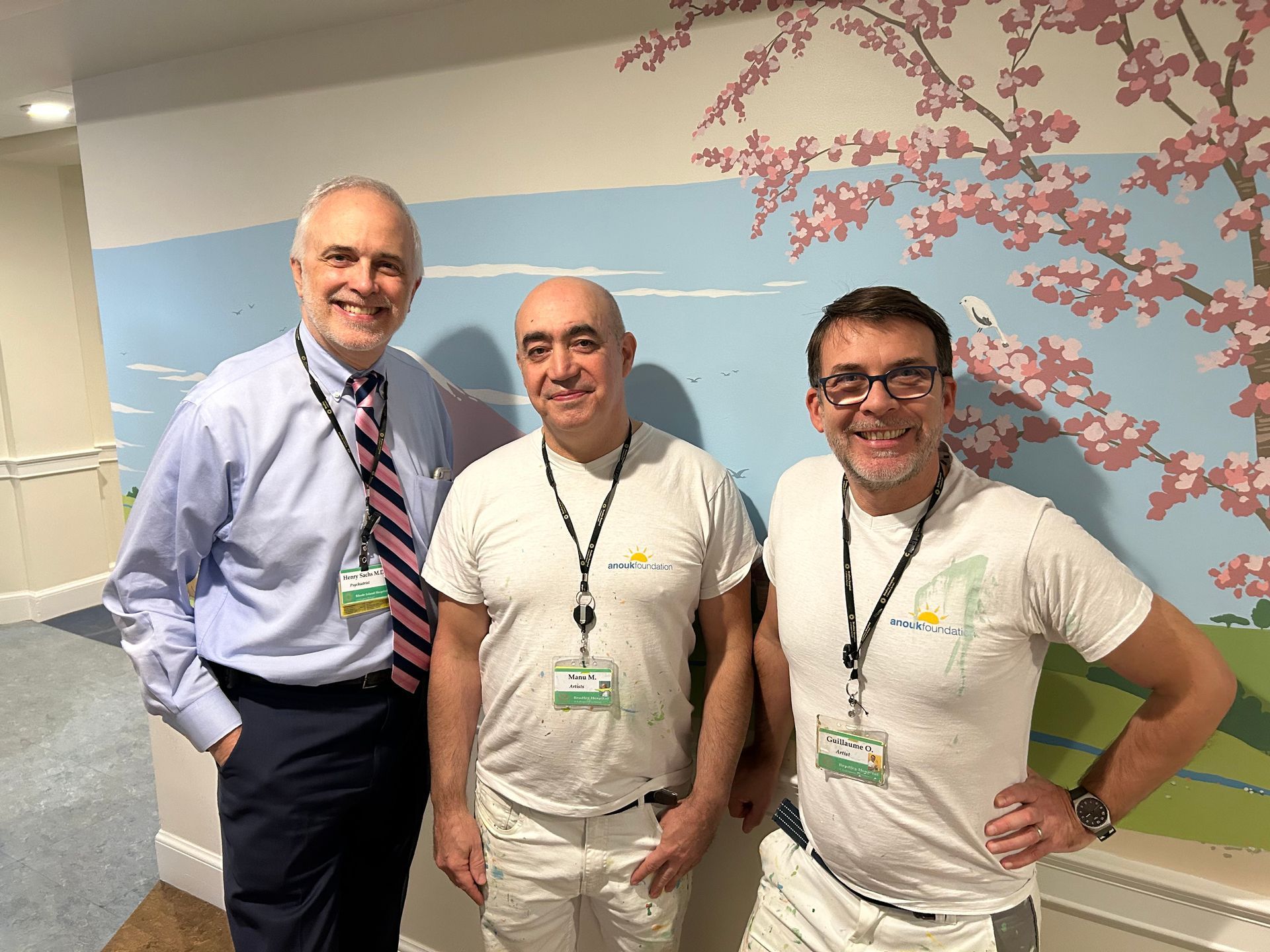 Three smiling coworkers standing in a hallway with a cherry blossom mural behind them